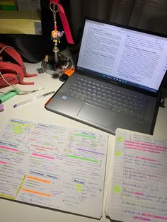 an open laptop computer sitting on top of a desk next to notebooks and pens