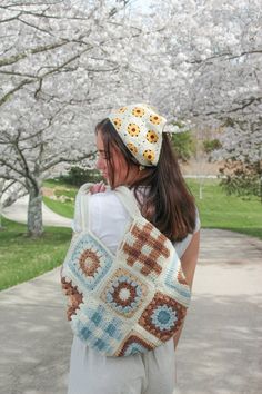 a woman carrying a crocheted granny bag in front of cherry trees with white blossoms