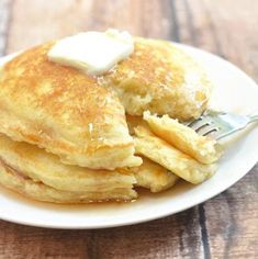 a stack of pancakes with butter on top and a fork in the middle, sitting on a white plate