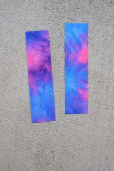 two pieces of blue and pink tie - dyed paper sitting on top of a cement wall