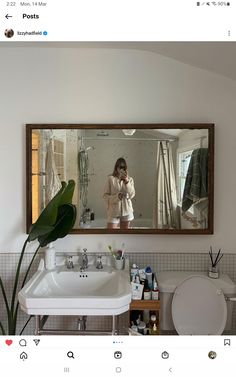 a person taking a selfie in a mirror above a sink and toilet with plants