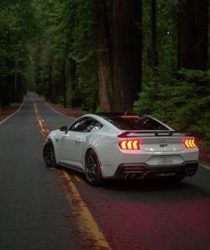 a white sports car is parked on the side of the road in front of some trees