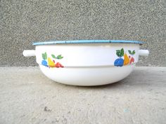 a bowl with fruit painted on it is sitting on the ground next to a wall