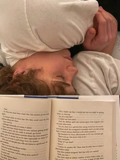 a person laying in bed with an open book over their head and reading it to someone else