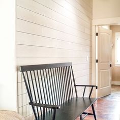 a black bench sitting in front of a white wall next to a door and wooden floor