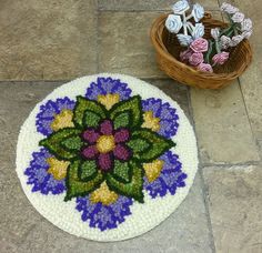 a crocheted flower rug next to a basket of flowers