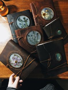 a person is holding a book with flowers on it and other leather books are sitting next to each other