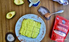 a plate with some food on it next to two cups of coffee and an avocado