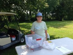 a woman standing next to a table with plastic containers on top of it and a golf cart in the background