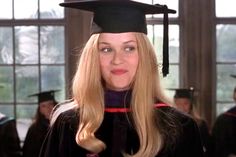 a woman with long blonde hair wearing a graduation cap and gown in a room full of people