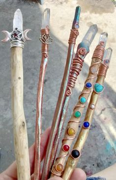 a person holding four different types of metal items in their hands, all with colored stones on them