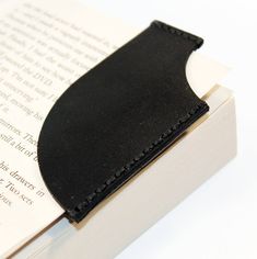 an open book with a black leather cover on it's edge, sitting on top of a white surface