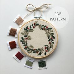 an embroidered wreath with holly leaves and red berries surrounded by spools of thread