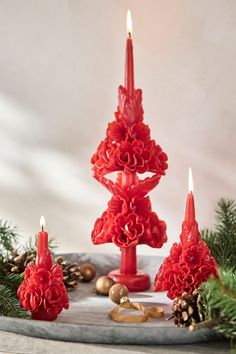 three red candles sitting on top of a table next to pine cones and christmas decorations