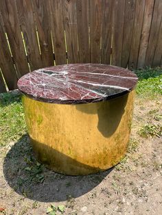 a round metal table sitting on top of a dirt field next to a wooden fence