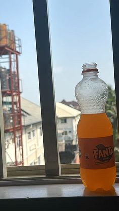 a bottle of orange juice sitting on top of a window sill next to a building