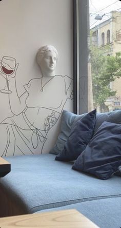 a blue couch sitting in front of a window next to a wall with a drawing on it