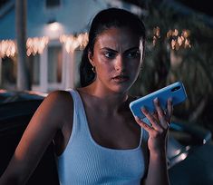 a woman in white tank top holding up a blue cell phone and looking at the camera