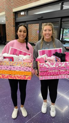 two girls are holding pink boxes with items in them and one girl is smiling at the camera