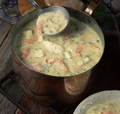 a pot filled with shrimp and cheese soup on top of a wooden table next to a plate