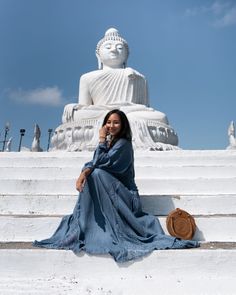 a woman sitting on the steps in front of a large buddha statue talking on her cell phone