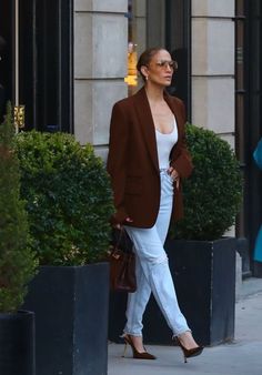 a woman walking down the street in white jeans and a brown blazer jacket with heels