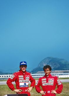 two men standing next to each other in front of a field with a skateboard