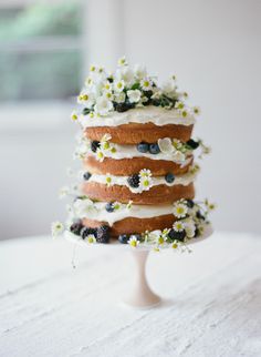 a three layer cake with berries and flowers on top