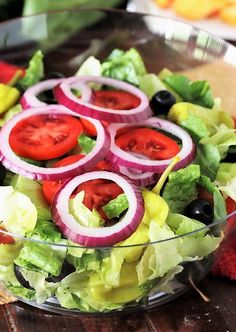 a salad with onions, tomatoes and lettuce in a glass bowl on a wooden table