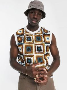 a man in a hat is standing with his hands on his hips and wearing a crocheted shirt