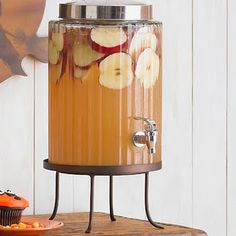 a beverage dispenser with apples and oranges in it on a table