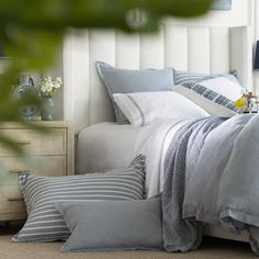 a bed with grey and white linens in a bedroom next to a nightstand filled with flowers