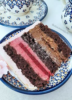 a piece of cake on a blue and white plate next to two teacups