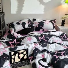 a laptop computer sitting on top of a bed covered in pink and black sheets with stars