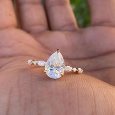 a person's hand holding an engagement ring with a pear shaped diamond on it