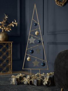 a gold christmas tree with blue balls and stars on it in front of a black wall