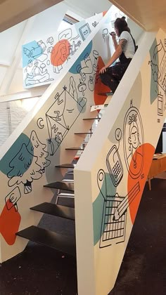 a woman climbing up the stairs in a building with drawings on it's walls