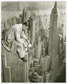 a man sitting on top of a tall building looking at a book in his hands