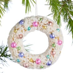 a christmas wreath ornament hanging from a pine tree with colorful ornaments on it