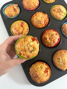 a hand is holding a muffin in a cupcake pan with other muffins