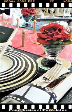 a table set with plates, silverware and red roses in a vase on it