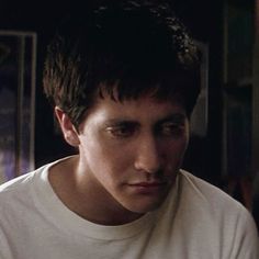 a young man in a white t - shirt stares at the camera