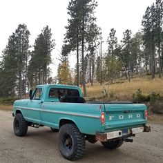 an old ford truck parked on the side of a dirt road in front of trees