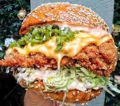 a chicken sandwich with lettuce, cheese and sauce is held in someone's hand