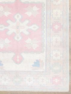 a pink and blue rug with an intricate design on the top, in front of a wooden floor