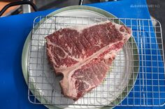 two pieces of steak on a plate sitting on a blue tablecloth next to a wire rack