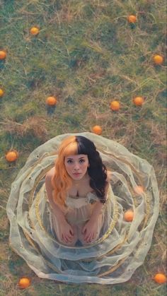 a woman sitting on the ground surrounded by oranges