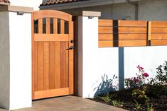 a wooden door on the side of a white building with flowers in front of it