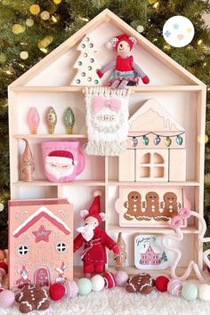 a wooden doll house with christmas decorations and ornaments on the floor next to a christmas tree