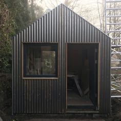 a small metal building with two windows and a ladder next to it in the woods